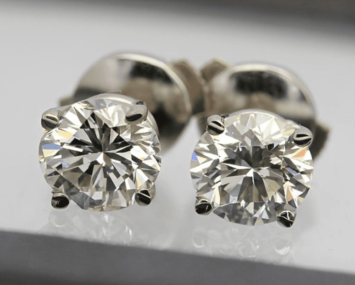 Diamond stud earrings on reflective surface.