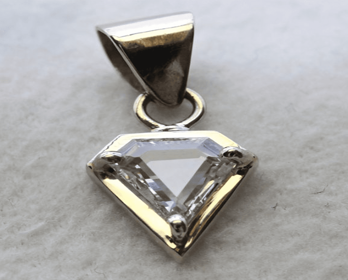 Diamond-shaped silver pendant on gray background.