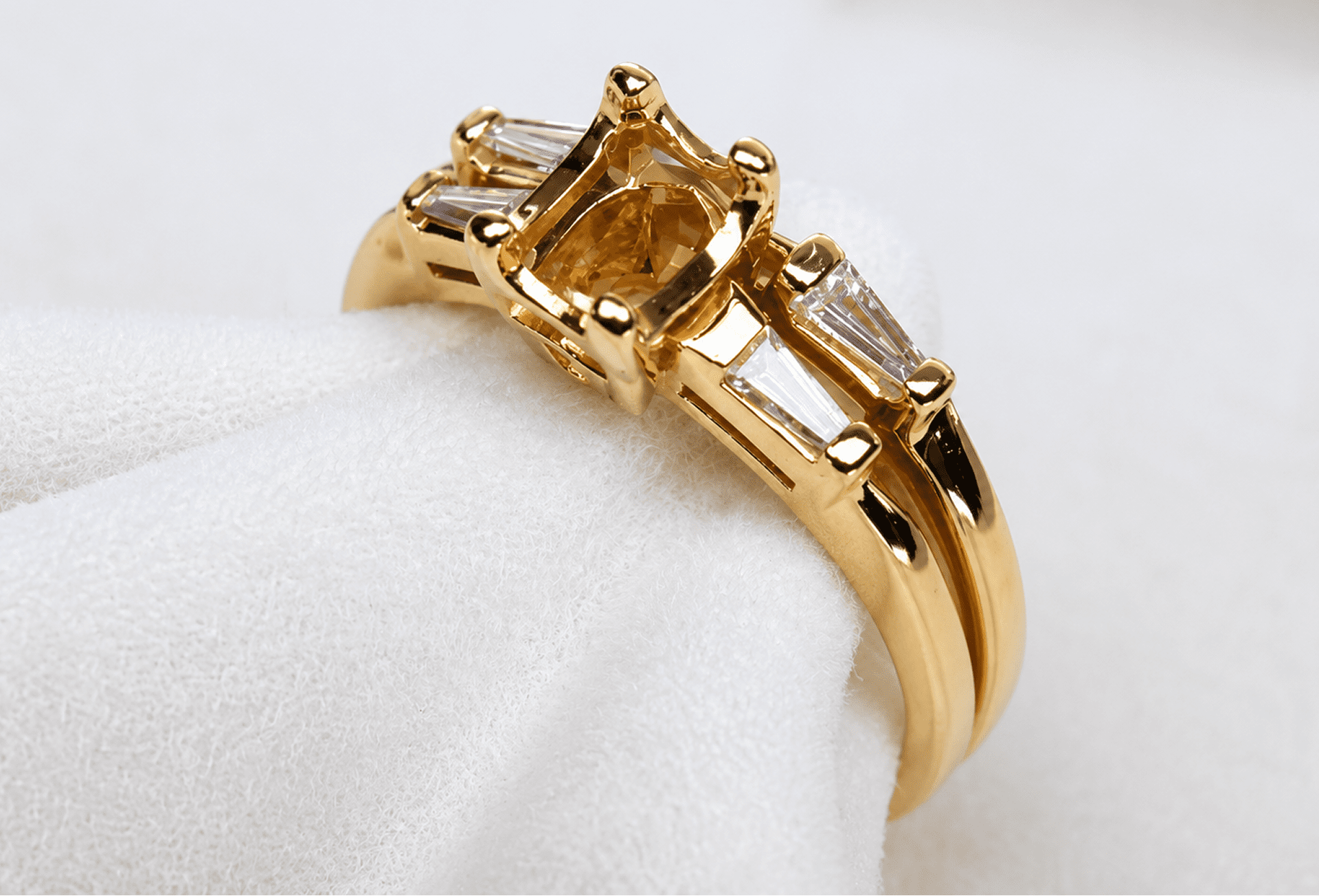 Gold ring with a square amber gemstone and tapered baguette side stones, displayed on soft white fabric.